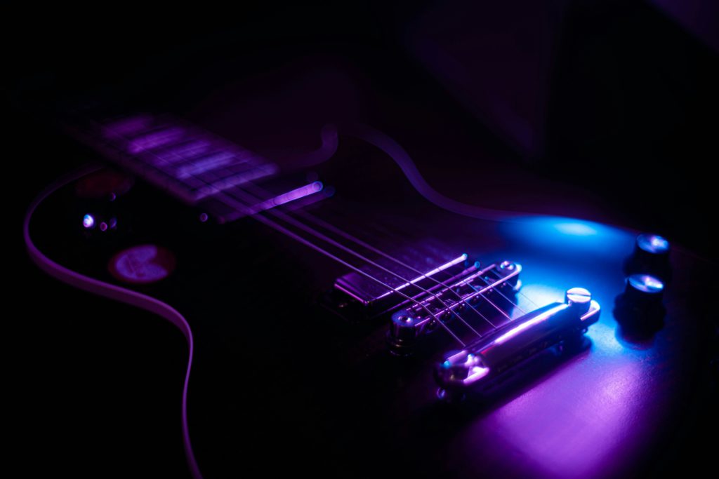 Close-up of an electric guitar in low light, highlighting the strings and body with a purple and blue glow. To represent the evolution of amplifiers